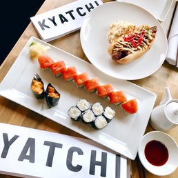 Kyatchi signature dishes Sustainably sourced Nigiri and Sashimi, Hotate Moto (scallops with spicy mayo & masago), Pork Belly Buns (Kakuni), Kyatchi Dog (Japanese hot dog), creative sushi rolls.